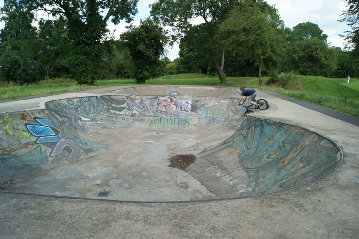 A child riding on a bike down a skate park ramp.